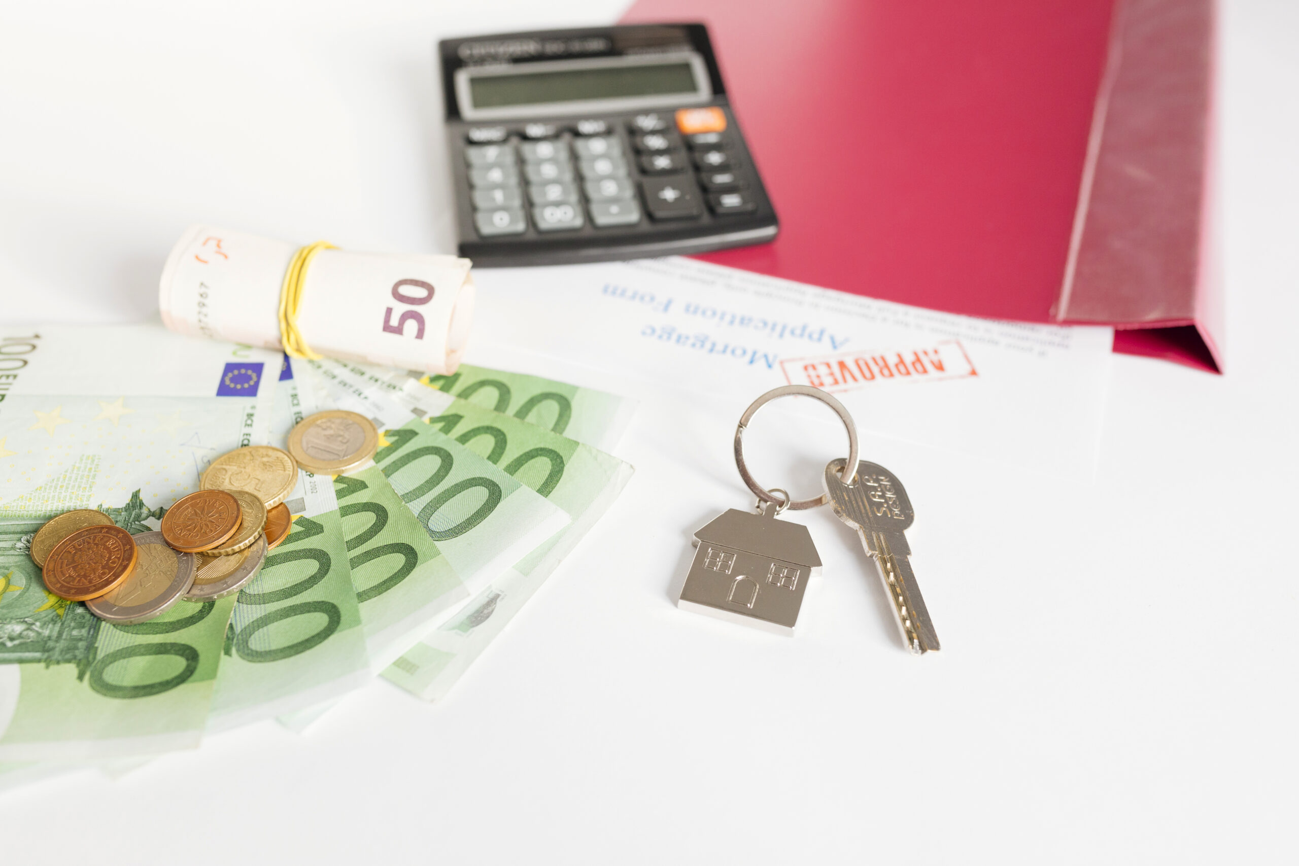Une calculette posée sur un contrat de prêt immobilier avec de l'argent et une clé sur un porte-clé maison